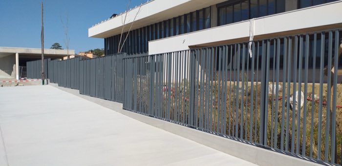 Clôture à lames verticales gris anthracite sur muret béton, devant un bâtiment public