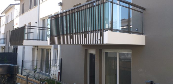 Garde-corps de balcon à remplissage verre et brise-vue à lames verticales, sur un immeuble contemporain