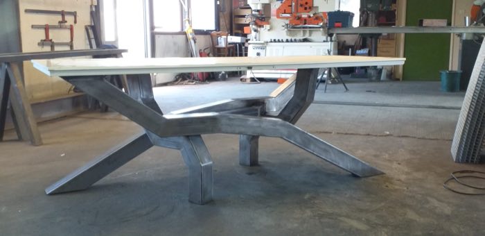 Table à plateau clair sur piétement en acier brut à branches obliques, à l'atelier
