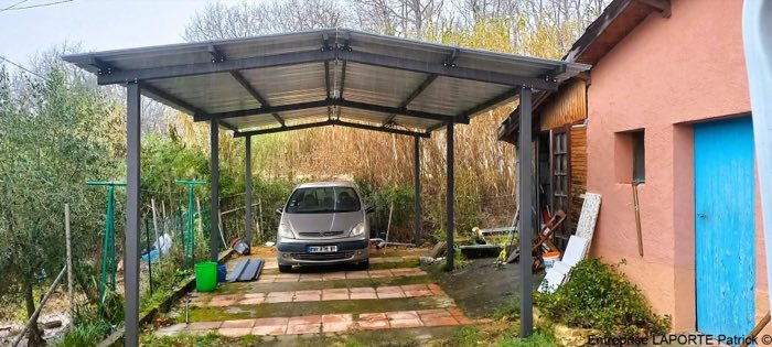 Carport anthracite à toiture translucide abritant une voiture, adossé à une dépendance
