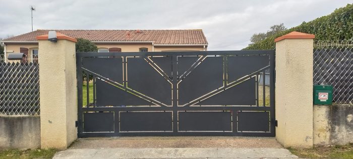 Portail battant gris anthracite à découpes en éventail, entre deux piliers crépis, devant une maison de plain-pied