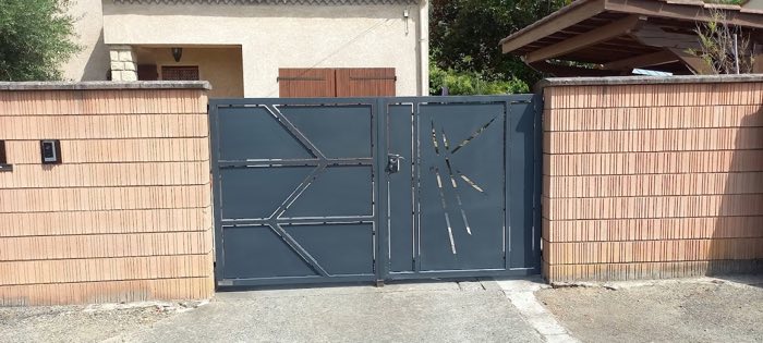 Portail battant gris anthracite à découpes graphiques ajourées, avec portillon intégré, sur un mur de brique